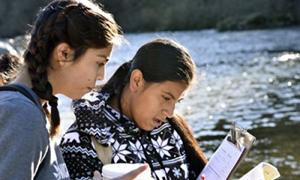 Two teenagers sitting by a lake and reading 
